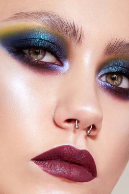 Parlak, yaratıcı makyajlı ve kafasında örgüler olan genç bir kız. Amazon suretinde parlayan derisi ve burnunda küpesi olan güzel bir manken. Güzel surat. Kapat.