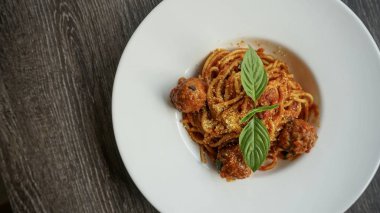 Ahşap masa üzerinde beyaz tabak içinde fesleğen yaprakları tarafından tepesinde köfte domates soslu spagetti 