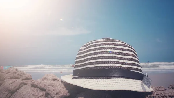 Hipster hat on sand against blurred image background of beach and blue sky, summertime concept