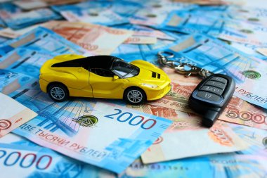 Sarı oyuncak araba, Rus para birimlerinin arka planında alarm. Kredi kartıyla ve taksitle yeni bir araba almak. Hediye arabası.