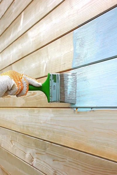 To paint the house. A man\'s hand in a work glove applies building acrylic paint to a wooden wall from boards.