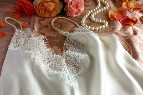 在缎子的床上用品上 躺着一条白色花边 珍珠项链和橙色珊瑚玫瑰的女式睡衣 — 图库照片