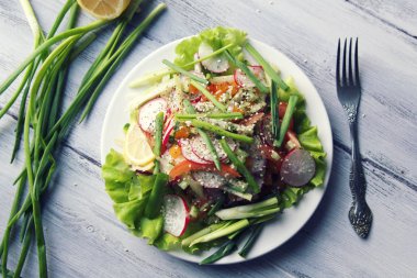 Bahar beyaz tabakta sebze salatası. Turp, domates, kereviz ve salatalık. Susam ile tepesinde. Beyaz ahşap masa üzerinde vejetaryen yemek. Yakın çekim. Üstten Görünüm.