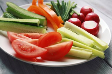 Beyaz tabak sebze vejetaryen salata için ile. Turp, domates, kereviz, biber, soğan ve salatalık. Beyaz ahşap mutfak masasında. Yakın çekim.