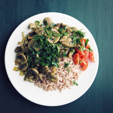 Kırmızı Pirinç mantar ve kiraz domates. Vegan yemek. Avrupa mutfağı. Siyah arka plan üzerinde basit sağlıklı öğle yemeği. Vejetaryen pirinç beyaz tabak çanak. Yakın çekim. Tonda fotoğraf. Üstten görünüm.