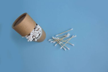 Mavi arka planda yeniden kullanılabilir kağıt ambalaj tüpündeki bambu pamuk çubuklarının üst görüntüsü. Tasarım ve modellemeleriniz için kopyalama alanı, sıfır atık kavramı