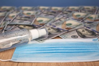 Tek kullanımlık yüz maskesi ve antiseptik sprey ya da arka planda kopyalanmış kağıt para banknotlarıyla dezenfekte edici. Para aklama veya tıpta rüşvet kavramı, Coronavirus sırasında yolsuzlukla mücadele