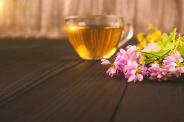 Çiçekler, yonca yaprakları ve ıhlamur yaprakları. Arkasında da doğal ahşap arka planda, kopyalanmış bir fincan taze bitki çayı var. Alternatif folk tıp konsepti, seçici odaklanma.