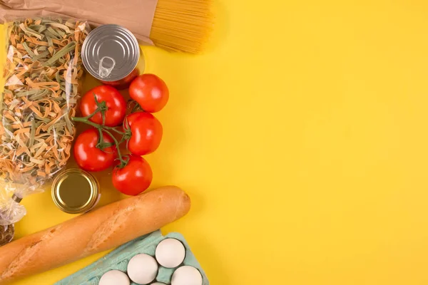 Flat lay composition with food donations on yellow background with copyspace - pasta, fresh vegatables, canned food, baguette, eggs, organic oil. Donation or contactless delivery food concept