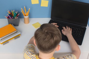 Çocuk karantina sırasında online çalışmak için dizüstü bilgisayar kullanıyor. Masada oturuyor. Evde eğitim, çevrimiçi eğitim dersleri veya eğitim teknolojisi kavramı