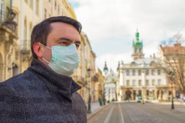 Coronavirus veya Covid-19 pandemisi sırasında boş sokağa karşı tek kullanımlık tıbbi maske takan yakışıklı genç bir Avrupalı. Yeni normal ve sosyal uzaklık kavramı