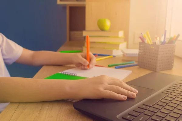 Schoolboy studying online using his laptop during online lesson or training classes, sitting at wooden table near window. Distance or home education and online studying concept. Back to school