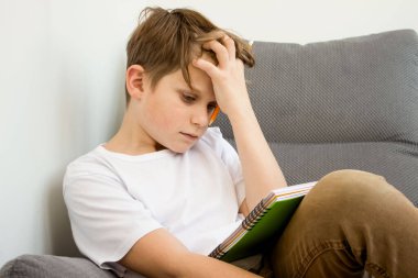 Evde ev ödevlerini zar zor yapan yorgun okul çocuğu sıkılmış, hayal kırıklığına uğramış ve dalmış. Evde kitaplarla çevrimiçi ders çalışmak. Çevrimiçi eğitim ya da kişisel eğitim kavramı. Okula geri dön.