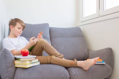 Öğrenci kanepede oturmuş kitap okuyor. İnternetteki karantina çalışmaları sırasında evdeki derslere hazırlanıyor. Çevrimiçi eğitim ya da kişisel eğitim kavramı. Okula geri dön.