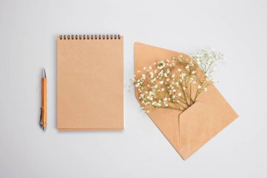 Pastel gri arka planda, ahşap kalem, kraft defter ve kraft kağıt zarf ile güzel, düz konum telif alanı ile. Tatil alışveriş listesi, gelinlik listesi veya Yeni Yıl Hedefleri konsepti