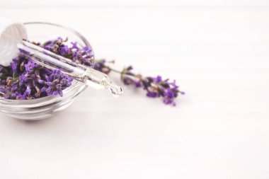 Etrafında lavanta yağı ve lavanta çiçekleri olan bir damlacık..