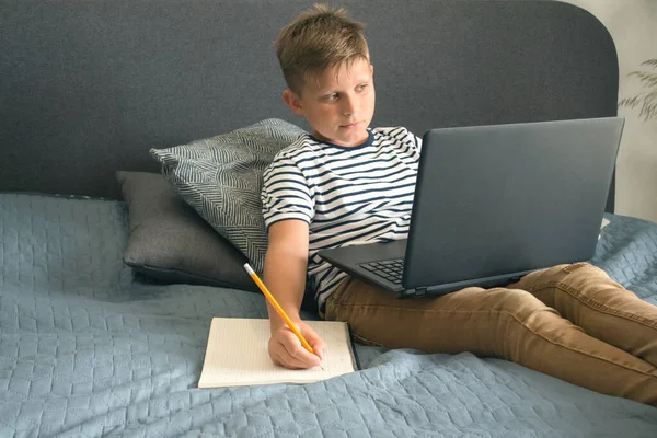 Retrato de vista frontal de un estudiante diligente escribiendo o dibujando, sentado en un sofá gris mientras hace la tarea. Estudiar en línea durante la cuarentena o concepto de educación personal. Plan de educación personal — Foto de Stock