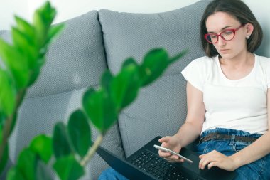 Genç bir iş kadını ya da öğrenci cep telefonu ve siyah dizüstü bilgisayarla evde çalışıyor ya da okuyor. Evden ya da online eğitim konseptinden uzaklık çalışması. Seçici odak