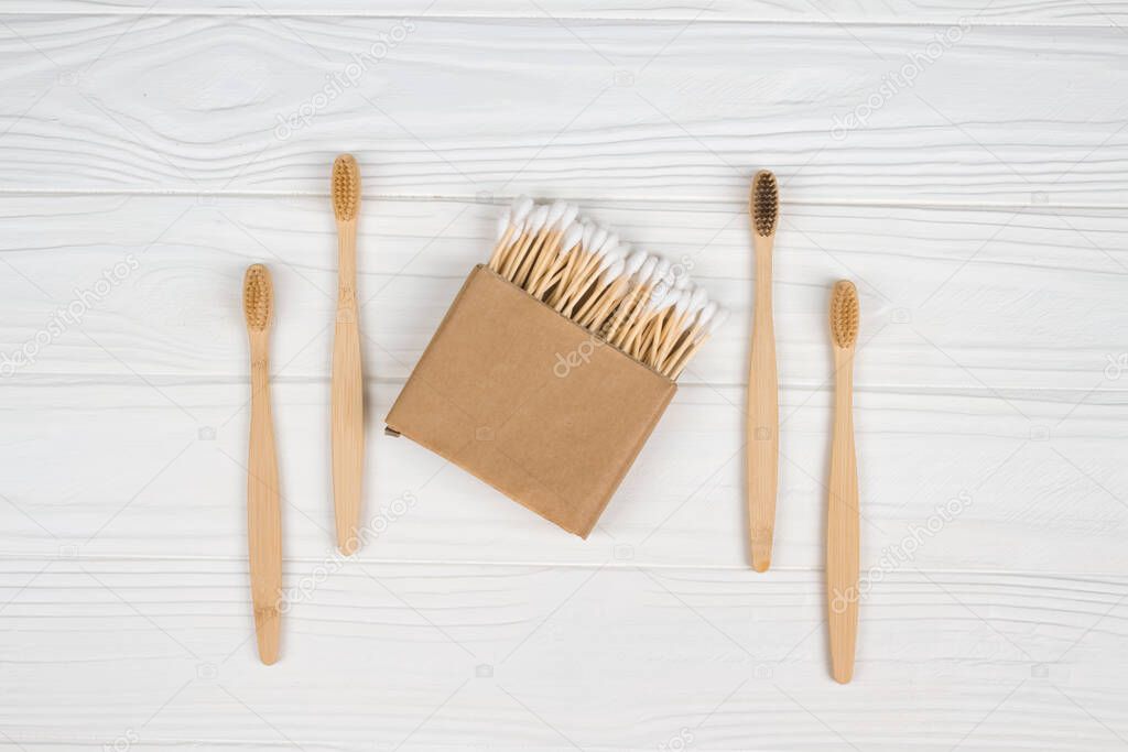 Cotton buds in kraft paper box and natural bamboo toothbrushes on white wooden background - zero waste bathroom essentials. Sustainable lifestyle concept. Mockup and copyspace