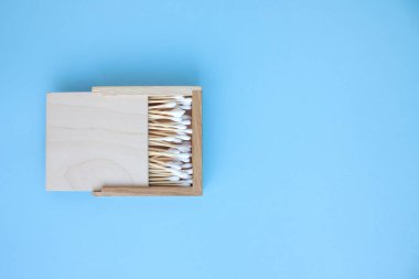Bambu pamuk tomurcuklarının mavi arka plandaki ahşap kutuda kopyalanmış görüntüsü. Sıfır atık ve sürdürülebilir yaşam tarzı konsepti, çevre dostu banyo esasları