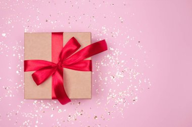 Kırmızı fiyonklu hediye kutusu, pembe arka planda altın parıltılar ve metin için kopyalanmış boşluk. Düz yatış stili. Noel, Yeni Yıl, Sevgililer Günü ya da doğum günü kutlaması konsepti