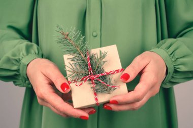 Yeşil elbiseli genç bir kadın Noel ağacı dallarıyla süslenmiş hediye kutusunu tutuyor. Noel tatili ve yeni yıl kutlaması konsepti. Noel için aile hediyeleri hazırlıyorum.