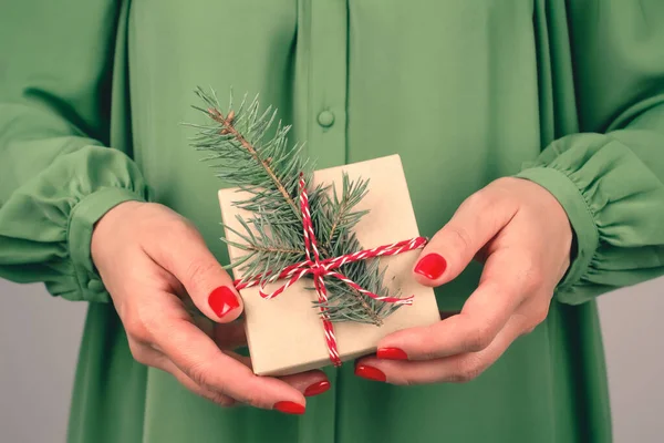 Yeşil elbiseli genç bir kadın Noel ağacı dallarıyla süslenmiş hediye kutusunu tutuyor. Noel tatili ve yeni yıl kutlaması konsepti. Noel için aile hediyeleri hazırlıyorum.