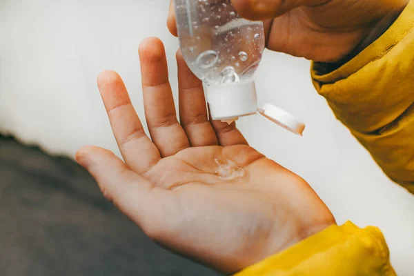 Egy gyerek sárga kabátban. A kezében egy üveg gél feldolgozására kezek baktériumok és vírusok. Alkoholtartalmú fertőtlenítő szer. — Stock Fotó
