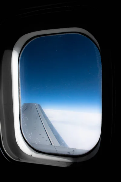 Lentokoneen porttireikä, jossa on siipi ja sininen taivas. Lentää pilvien ja maan päällä.. — kuvapankkivalokuva