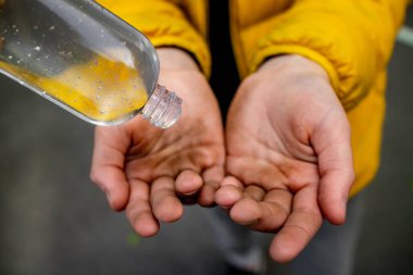 Çamura batmış bir çocuğun elleri. Temizlemek için temiz plastik jel şişesi. Bakteri ve virüslere karşı antiseptik.