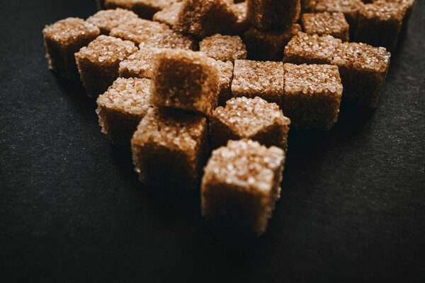 Brown cane sugar in cubes on a black background. Still life. Carbohydrates and non-diet food. Calories.