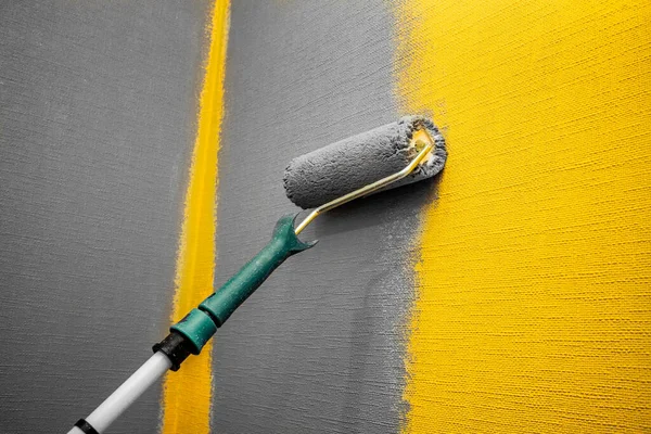 Close up roller with gray paint for painting walls. Repairs. Yellow wall. Background. Screensaver for the site. — Stock Photo, Image