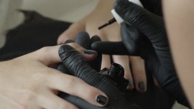 Siyah lateks koruyucu eldivenlerin ustası fırçayı siyah cila ile tüpe batırıyor. Güzellik Salonu, Manikür