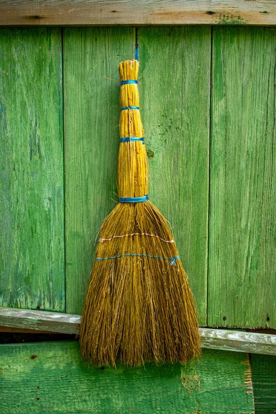 Uma vassoura de limpeza encostada a uma parede de madeira verde de uma casa velha. Produtos de limpeza para uso doméstico. Vila. — Fotografia de Stock