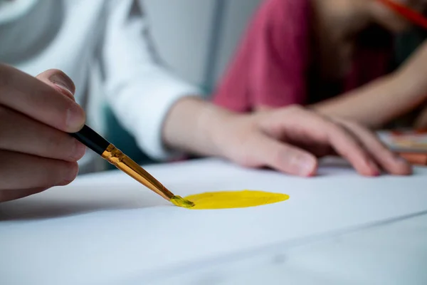 Barnens hand ritar gul sol på vitt papper. Ritar lektioner i skolan. Hemundervisning. Konst. Närbild av en borste. — Stockfoto