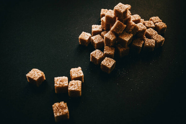 Brown cane sugar in cubes on a black background. Still life. 