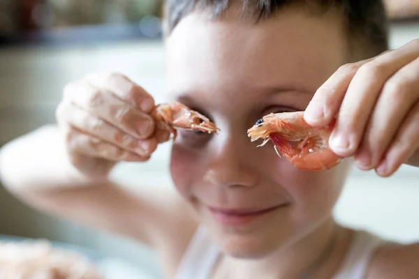 Menino coloca dois camarões em seus olhos como óculos e sorrisos — Fotografia de Stock