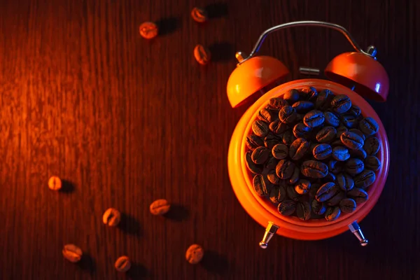 Reloj despertador naranja con granos de café en una mesa de madera — Foto de Stock