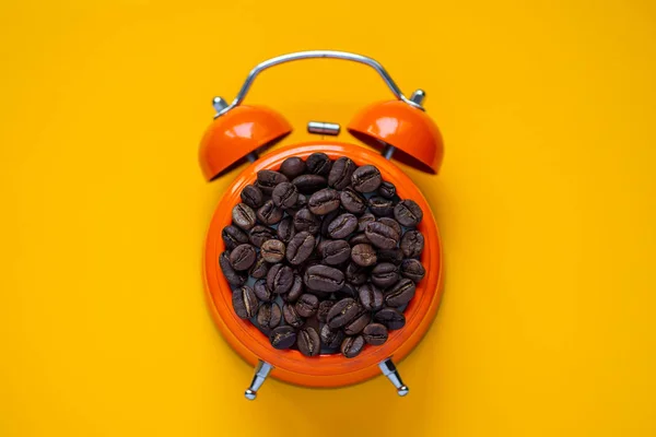 黄色の背景にオレンジ色の目覚まし時計でコーヒー豆 — ストック写真