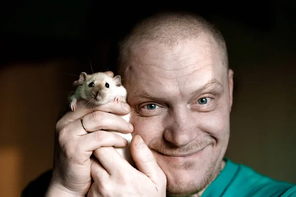 En man håller en råtta i famnen och ler — Stockfoto