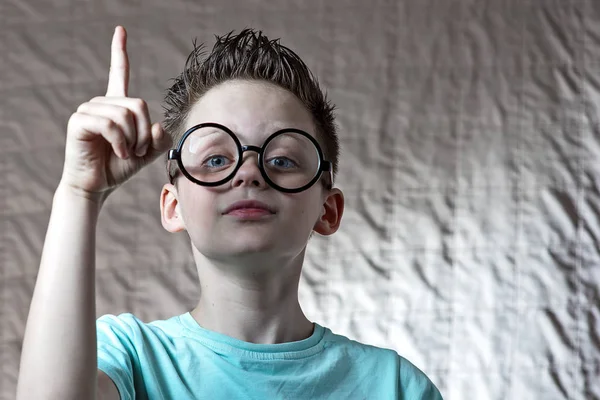 En dreng i en let t-shirt og runde briller løftede pegefingeren - Stock-foto