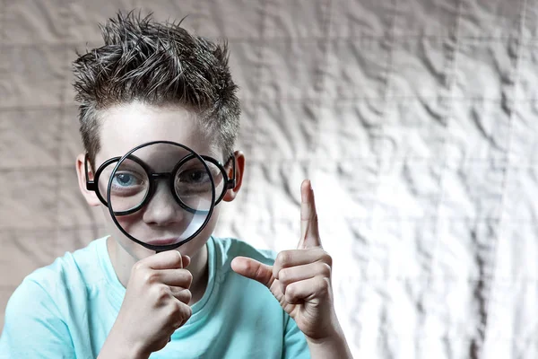 Niño en una camiseta ligera y gafas mirando en una lupa grande — Foto de Stock