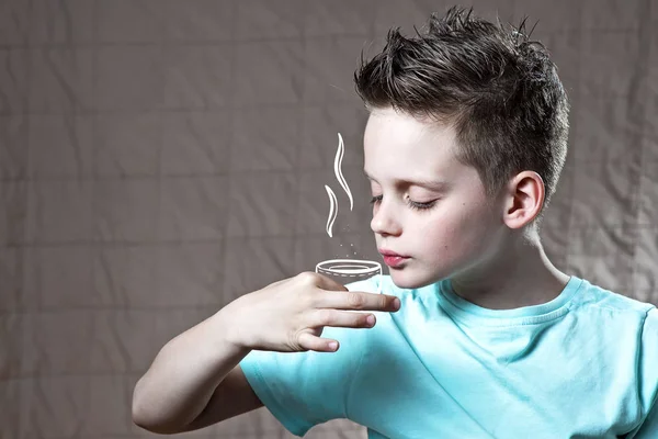 Niño en una camiseta ligera sosteniendo una taza pintada de té o café — Foto de Stock