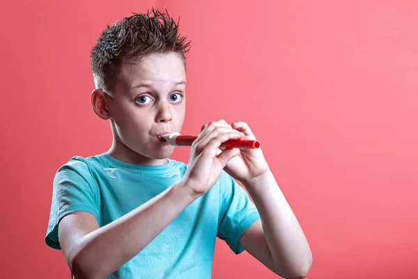 En dreng i en let t-shirt, der spiller på et rør på en farvet baggrund - Stock-foto