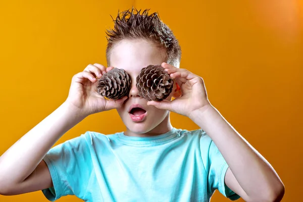 En dreng i en let t-shirt satte to kegler til hans øjne på en farvet baggrund - Stock-foto