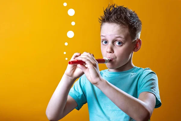 En dreng i en let t-shirt, der spiller på et rør på en farvet baggrund - Stock-foto