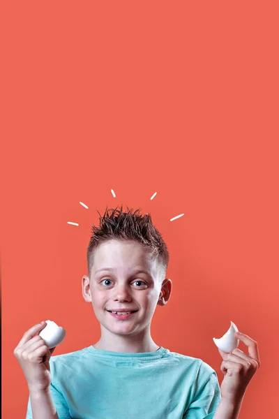 Menino alegre em uma camiseta leve segurando um ovo quebrado em um fundo colorido — Fotografia de Stock