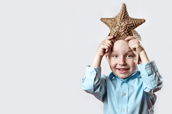 Niño en una camiseta ligera sosteniendo una estrella de mar sobre un fondo blanco — Foto de Stock