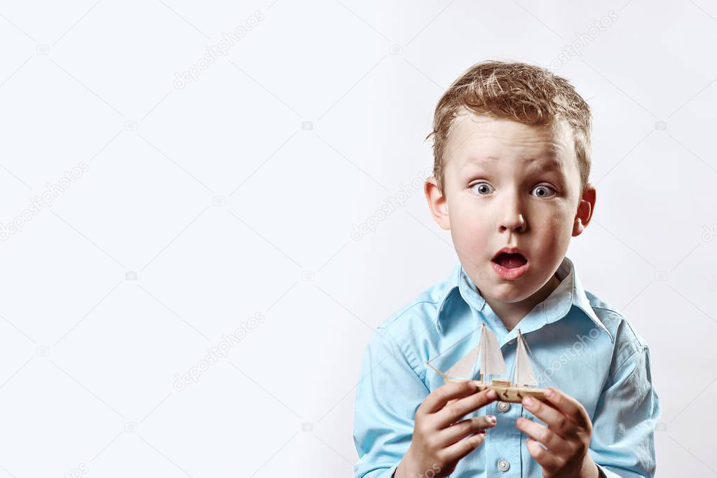 a surprised boy in a blue shirt holding a boat in his hands on a light background