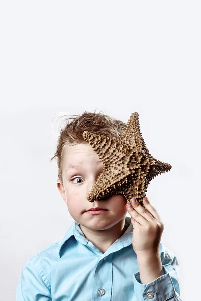 Niño en una camiseta ligera sosteniendo una estrella de mar sobre un fondo blanco — Foto de Stock